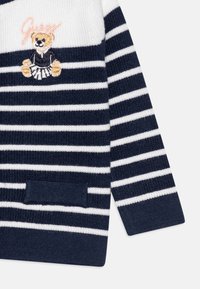 Suéter a rayas en azul marino y blanco con bordado de un oso, textura acanalada y un bolsillo frontal. Material de punto suave con un corte holgado.
