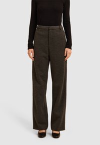 Pantalons larges gris foncé en tissu texturé, avec une taille ajustée et des pinces subtiles à l'avant, associés à des chaussures noires.