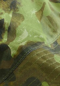 Grüner Tarnstoff mit unterschiedlichen Schattierungen von hellgrün und dunkelgrün, der eine strukturierte Webart und sichtbare Nähte entlang der Kanten aufweist.