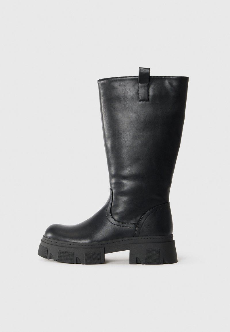 Botte en cuir noire mi-mollet avec semelle crantée épaisse et attache sur le côté, présentée en profil sur un fond blanc.
