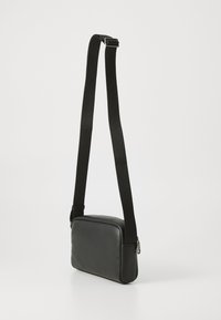 Sac à bandoulière en cuir noir avec une texture lisse, de forme rectangulaire, sangle noire réglable et détail de fermeture éclair en argent.