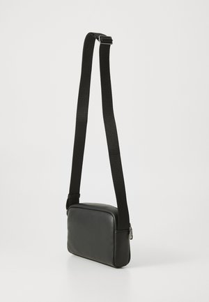 Melns ādas plecu soma ar gludu tekstūru, taisnstūra formu, regulējamu melnu siksnu un sudraba rāvējslēdzēja detaļām.