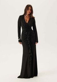 Černé dlouhé šaty s dlouhým rukávem z měkké látky, s hlubokým výstřihem do V, volánkovými detaily na přední straně a květinovými ozdobami v pase.