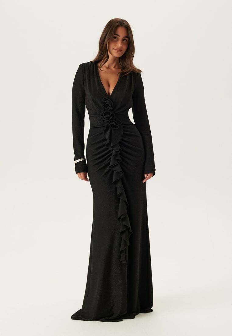 Černé dlouhé šaty s dlouhým rukávem z měkké látky, s hlubokým výstřihem do V, volánkovými detaily na přední straně a květinovými ozdobami v pase.