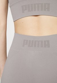 Top sportivo grigio a maniche corte e leggings a vita alta in tessuto testurizzato con logo PUMA di una tonalità leggermente più scura. Design senza cuciture, vestibilità elastica.
