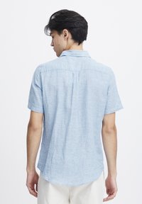 Camicia a maniche corte con colletto in tessuto blu chiaro con finitura testurizzata. Presenta un dettaglio con yoke sul retro e un orlo curvo.