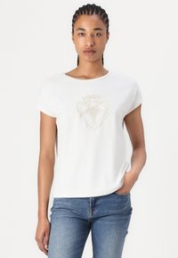Valkoinen lyhythihainen t-paita pyöreällä pääntiellä, jossa on hienovarainen beige graafinen kuvio keskellä. Valmistettu pehmeästä kankaasta, rento istuvuus.