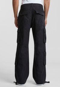 Svarta cargobyxor med lös passform, som har flera sidofickor, raka ben och justerbara ankle straps. Tillverkade av slitstarkt tyg.