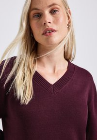 Pull en tricot bordeaux avec un design en V, présentant des détails côtelés au niveau du col et une surface texturée. Conception de sweat-shirt.