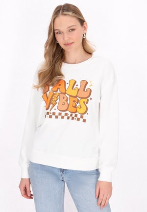 Felpa bianca con una grande grafica arancione e marrone che recita "FALL VIBES" con un motivo a scacchi e stelle decorative nella parte inferiore.