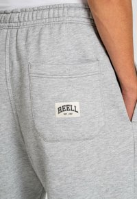 Graue Jogginghose mit einer Gesäßtasche und einem gestickten Logo-Patch mit der Aufschrift "REELL EST. 1997." Hergestellt aus weichem Material mit glatter Textur.