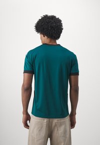 Turkos t-shirt med kort ärm och mörka detaljer på krage och ärmar. Har en avslappnad passform och är tillverkad av mjukt, lätt material.