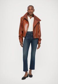 Chaqueta de cuero marrón corta con cuello ancho, suéter blanco de canalé, jeans rectos de mezclilla azul oscuro y bailarinas negras. Textura suave y diseño ajustado.