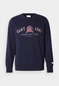 Kék garbó, pamutból készült, kerek nyakkivágással, hosszú ujjal és grafikus nyomattal, amelyen "GANT 1949" �és "AMERICAN SPORTSWEAR" felirat található.