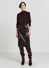 Haut bordeaux à manches longues avec un col drapé, associé à une jupe en cuir brillante, fendue, longueur genou, et des bottes hautes jusqu'à la cuisse, ajustées et vernies.