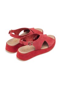 Red suede wedge sandals with crossed straps and a buckled ankle closure. Cushioned footbed with gold embossed brand logo. Flat rubber sole.