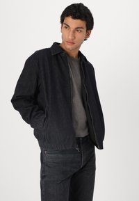 Black denim jacket with a ribbed hem, front pockets, and a collared neckline, paired with a dark grey textured T-shirt and jeans.