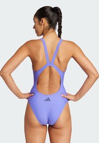 Fioletowy strój kąpielowy z dekoltem typu racerback, odkryty plecy i akcentem w postaci logo. Wykonany z gładkiego materiału o dopasowanej sylwetce, idealny do pływania.