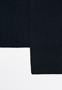 Tessuto a maglia nero a coste, superficie strutturata, con un bordo pulito, che mostra una transizione fluida verso uno sfondo più chiaro.