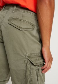 Oliivinvihreät työshortsit, joissa on useita taskuja, sileä pinta ja rento istuvuus. Vahvistetut saumat ja klassiset lahkeensuut.