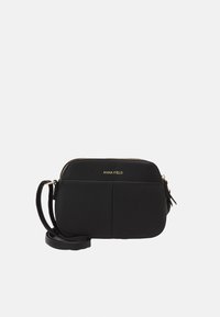 Černá crossbody taška vyrobená z hladkého syntetického materiálu, s zaoblenými hranami, zlatým zipem a logem značky na přední straně.
