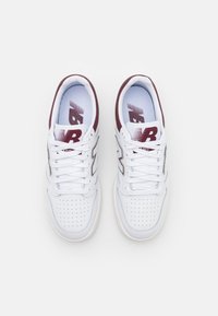 Zapatillas deportivas blancas con acentos burdeos, material de cuero, punta perforada, cordones planos y un talón reforzado. Logotipo de New Balance visible.
