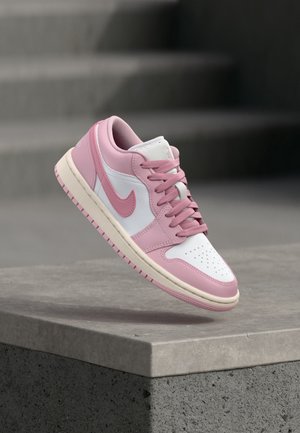 Baskets Nike roses et blanches avec lacets, flottant au-dessus d'un rebord en béton gris avec des marches floues en arrière-plan.