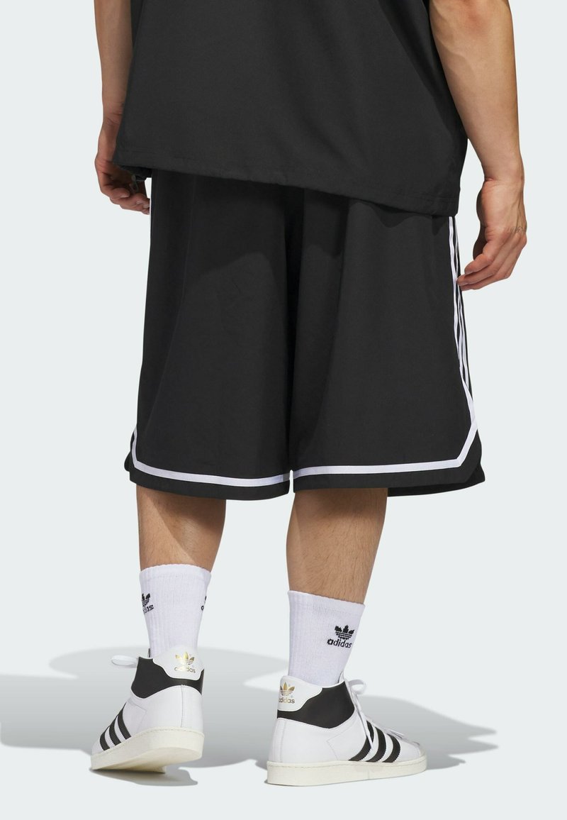 Shorts de sport noirs avec des accents blancs, présentant une coupe ample et une texture lisse. Portés avec des chaussettes blanches et des baskets noir et blanc.