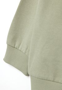 Tejido de sudadera verde con puños y dobladillo de canalé. Textura suave con un ligero estiramiento, mostrando un diseño limpio y moderno.