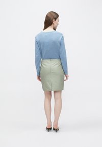 Camisola de malha azul clara com mangas compridas combinada com uma saia lápis de couro verde claro. Texturas suaves e silhueta ajustada.