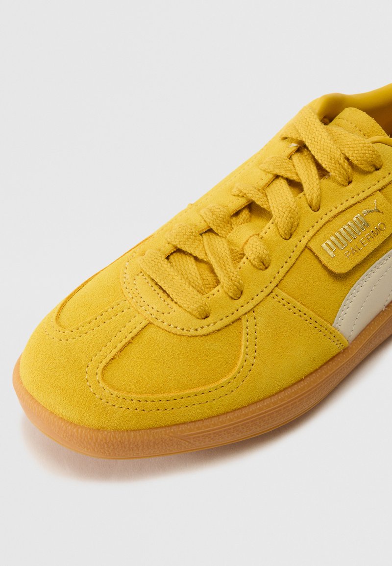 Gelbe Wildledersneaker mit glatter Textur, ausgestattet mit tonalen Schnürsenkeln, einer Gummisohle und silbernen Logoakzenten an der Seite.