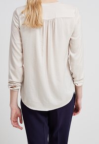 Camicia lunga beige chiaro con schiena arricciata, scollatura rotonda e maniche arrotolate; tessuto morbido e testurizzato; orlo curvo.