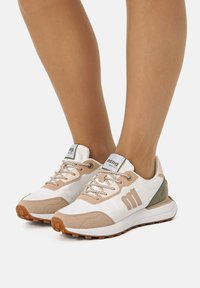 Baskets blanches et beiges avec des accents en daim texturé, des lacets plats et une languette à logo. Semelles en caoutchouc avec une accroche à motif.