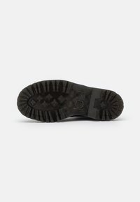 Black rubber outsole with deep tread pattern and textured surface; features branding and markings on the side.