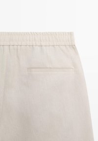 Beige fabric pants with elastic waistband and a single horizontal slit back pocket on the right side.