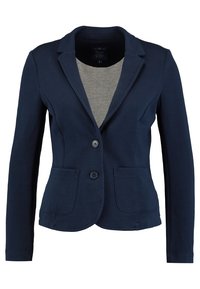 Marinblå kavaj i bomullsblandning med slagkrage, två framfickor och två knappstängningar. Långa ärmar.