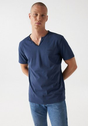 Camiseta de manga corta azul marina con escote en V y sutil detalle de costura. Fabricada con tela suave, presenta un ajuste relajado y estampado de logo.