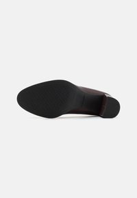 Zapato de cuero marrón con suela de goma negra texturizada. El tacón está ligeramente elevado, ofreciendo un diseño clásico y formal.
