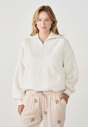 Witte fleece pullover met een kwart-rits kraag, voorzien van een geribbelde textuur panel en verlaagde schouders. Gepaard met pastelgestreepte broeken met bloemenborduursel.