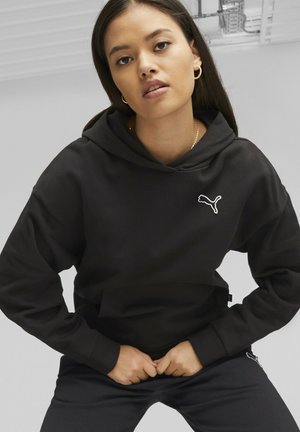 Felpa nera con cappuccio e logo Puma bianco sul petto, con una vestibilità comoda e tessuto testurizzato. Indossata con pantaloni neri abbinati.