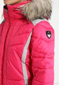 Pink puffer jacket with a furry hood, gray accents along the sleeves, quilted texture, and a logo patch on the right shoulder.