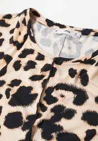 Blouse en imprimé léopard présentant un tissu doux, un col rond et des accents noirs sur un fond beige, avec des détails d'imprimé animal prédominants.