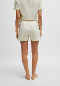 Krämfärgade, lätta shorts med elastisk midja, slät yta och avslappnad passform, i kombination med en matchande kortärmad topp.
