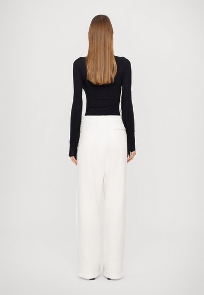 Black long-sleeve top with lace sides paired with white wide-leg trousers made from soft fabric. Simple design, neutral colors, relaxed fit.