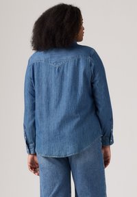 Denimhemd in mittelblau mit langen Ärmeln, Knopfmanschetten und abgerundetem Saum. Enthält ein Yoke-Design auf dem Rücken. Strukturierter Stoff.