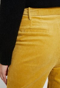 Gul kordbyxor med vertikala ribbor, med en bakficka och en bältesögla. I kombination med en svart, texturerad tröja.