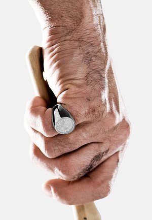 Schwarzer und silberner Ring mit einem kreisförmigen, erhabenen Design, der ein hölzernes Objekt hält; die Hand zeigt sichtbare Venen und eine leichte Textur.