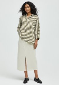 Striped, long-sleeve button-up shirt in olive green and cream, paired with a cream, mid-length skirt featuring a front slit and a smooth texture.