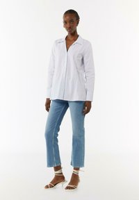  Lichtblauw gestreept overhemd met knopen en een kraag, gecombineerd met lichtdenim cropped jeans en witte strappy haksandalen.