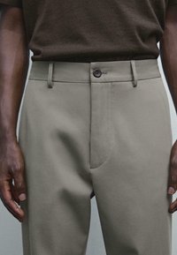 Pantaloni khaki a gamba dritta realizzati in tessuto morbido, con chiusura a un bottone, passanti per cintura e tasche laterali.